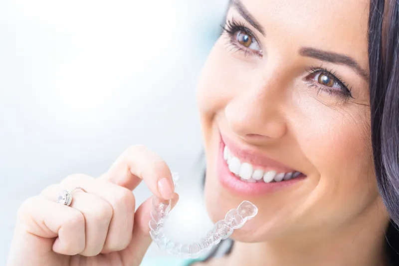 Paciente sonriendo mientras sostiene un alineador transparente para su tratamiento de ortodoncia invisible en Cuautitlán Izcalli.